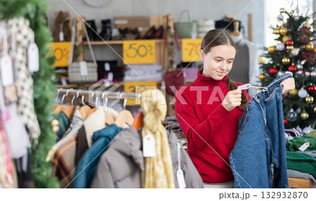 Teen girl is busy looking at clothes items in store, she choose jeans trousers 132932870
