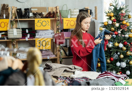 Teenage girl chooses jeans trousers in clothing store 132932914
