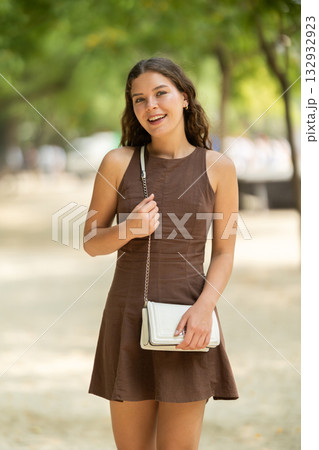 Pretty young woman in summer dress with handbag walking and posing in park on spring day Pretty young woman in summer dress with handbag walking and posing in park on spring day 132932923