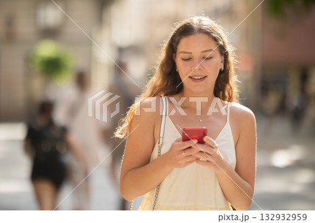 Young woman with phone walking along city street Young woman with phone walking along city street 132932959