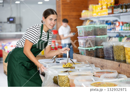 Young girl in supermarket, scooping marinated olives from bucket with ladle Young girl in supermarket, scooping marinated olives from bucket with ladle 132932971
