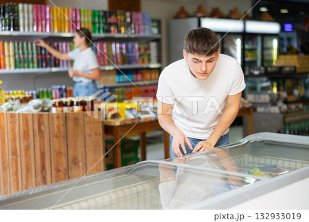 Guy chooses frozen semi-finished products in supermarket 132933019