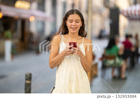 Happy young woman with mobile phone in her hands walking around city and taking pictures of sights Happy young woman with mobile phone in her hands walking around city and taking pictures of sights 132933084