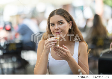 Smiling stylish young woman drinking espresso coffee sitting at cafe Smiling stylish young woman drinking espresso coffee sitting at cafe 132933085