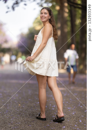 Cheerful girl in white dress walking along the street among architecture with bag Cheerful girl in white dress walking along the street among architecture with bag 132933149