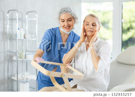 Satisfied old woman patient holding mirror sitting on clinical chair 132933257