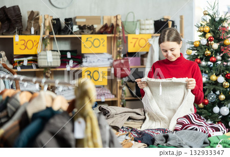 Teen girl picks up clothes and chooses sweater, New Year Eve sale 132933347