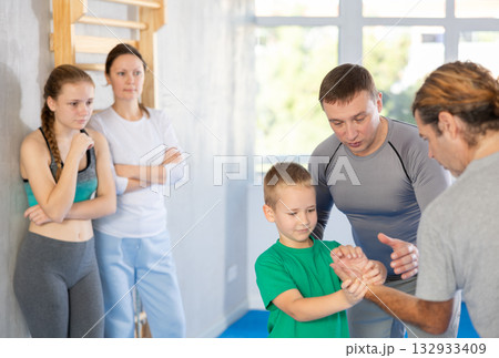Trainer on man explains palm grab technique, boy, girl and woman watch and learn Trainer on man explains palm grab technique, boy, girl and woman watch and learn 132933409