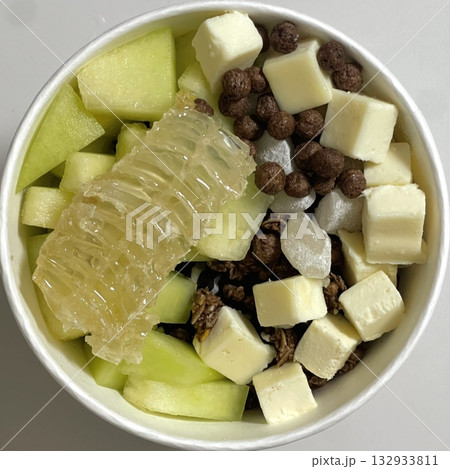 Swirled yogurt ice cream dessert served in a cup, smooth creamy texture with glossy surface, topped with fresh fruit pieces, highlighting its refreshing and inviting appearance in detail 132933811