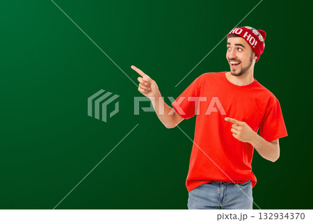 Young man in red shirt and festive hat pointing cheerfully 132934370