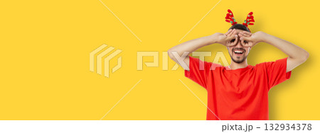 Young man playfully poses with hands around eyes wearing antlers Young man playfully poses with hands around eyes wearing antlers 132934378