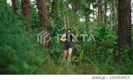 Energetic Young Woman Running Through Lush Green Forest Trail Surrounded by Tall Trees and Vibrant Nature in Bright Athletic Wear Energetic Young Woman Running Through Lush Green Forest Trail Surrounded by Tall Trees and Vibrant Nature in Bright Athletic Wear 132934853