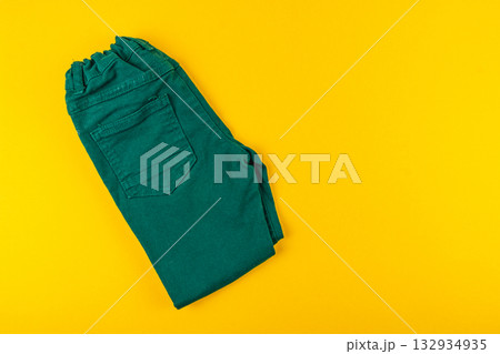 Colorful green pants folded neatly against a bright yellow background Colorful green pants folded neatly against a bright yellow background 132934935