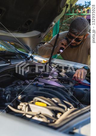 Man checking car engine with flashlight in afternoon light 132935028