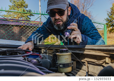 Man inspecting car engine under a clear sky in the countryside Man inspecting car engine under a clear sky in the countryside 132935033
