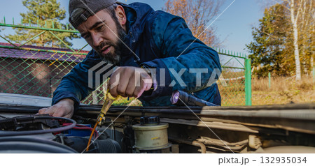 Man performs car maintenance in nature on a clear day 132935034