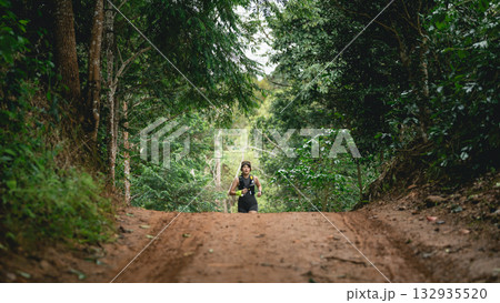 Person Running on a Dirt Path Through Lush Green Forest Surrounded by Trees and Natural Vegetation, Perfect for Outdoor Activity and Fitness Themes Person Running on a Dirt Path Through Lush Green Forest Surrounded by Trees and Natural Vegetation, Perfect for Outdoor Activity and Fitness Themes 132935520
