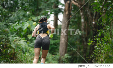 Female runner in sports gear jogging along a forest path surrounded by lush greenery, promoting health and fitness in an outdoor environment 132935522