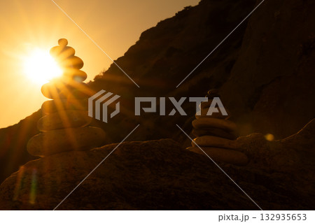 Balance stones sunset, silhouetted cairns stacked high against dramatic golden sky and rocky cliffs, illustrating meditation and tranquility. Balance stones sunset, silhouetted cairns stacked high against dramatic golden sky and rocky cliffs, illustrating meditation and tranquility. 132935653