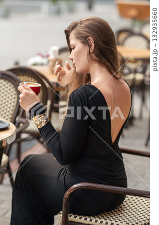 Coffee Dress Woman: Lady drinks coffee at outdoor cafe in elegant backless black dress. 132935660