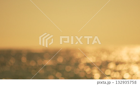 Bokeh Sunset Ocean: Golden sunlight shimmering on blurred ocean waves at dusk, creating sparkling reflections. 132935758