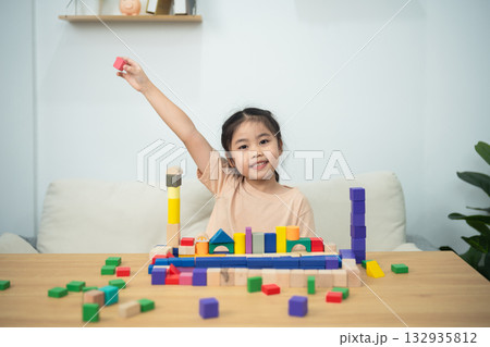 Happy child playing with colorful building blocks at home, creating structures and learning through play in a bright and inviting environment 132935812