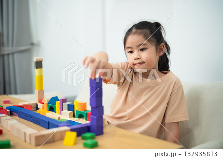 Young Girl Stacking Colorful Building Blocks in Bright Room, Engaged in Educational Playtime Activity, Developing Creativity and Motor Skills 132935813
