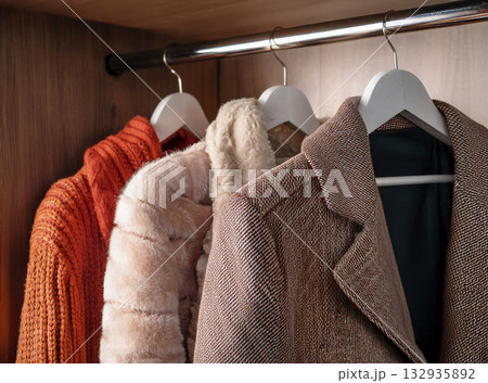 クローゼットに赤色茶色系のニットのコートとジャケットとセーター 132935892