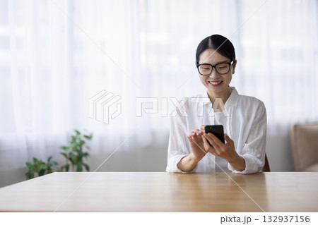 スマートフォンを笑顔で操作するメガネをかけたミドル女性 132937156