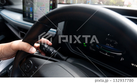 Close up fingers grip the steering wheel and move your fingers to control the turn signal lever. Interior of car with light of screen panel for navigator. blurred city on outside car. 132937780