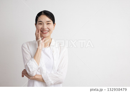 白い壁の前で顔に手を添えて微笑むミドル女性 白い壁の前で顔に手を添えて微笑むミドル女性 132938479