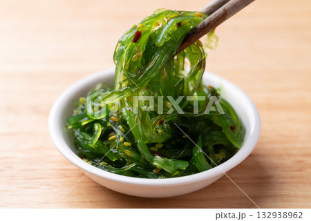 Wakame seaweed salad with sesame seed in a bowl with chopsticks on wooden background Wakame seaweed salad with sesame seed in a bowl with chopsticks on wooden background 132938962