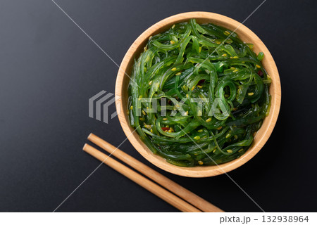 Wakame seaweed salad with sesame seed in a wooden bowl with chopsticks on black background, Top view 132938964