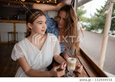 Women Cafe Latte Affection: Two women enjoy a latte and sweet treat at a cafe, sharing a tender moment. 132939558