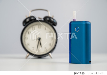 Electronic cigarette and alarm clock on white background. Tobacco heating systems. Electronic cigarette and alarm clock on white background. Tobacco heating systems. 132941300