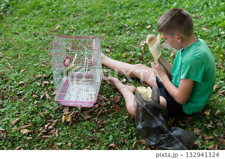 Boy cleaning his pet bird's cage outdoors. Boy cleaning his pet bird's cage outdoors. 132941324
