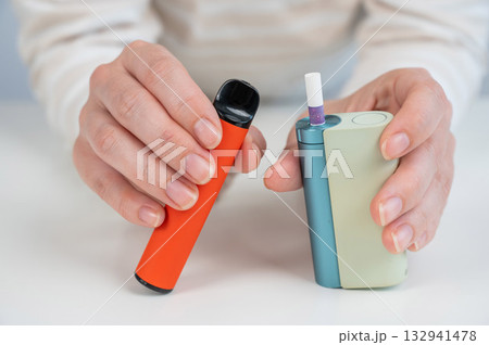 Woman holding electronic cigarette and disposable vape on white background. Tobacco heating systems and vaporizer.  132941478