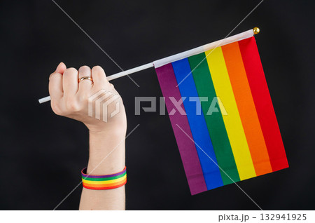 Woman with wedding ring holding rainbow flag on black background.  132941925