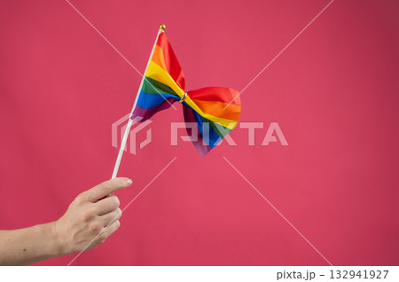 Woman holding rainbow flag fastened with wedding ring on pink background. Woman holding rainbow flag fastened with wedding ring on pink background. 132941927