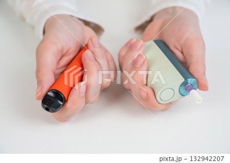 Woman holding electronic cigarette and disposable vape on white background. Tobacco heating systems and vaporizer. Woman holding electronic cigarette and disposable vape on white background. Tobacco heating systems and vaporizer. 132942207