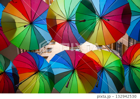 Colorful umbrellas create a vibrant display above a narrow street in a lively urban area during a sunny day 132942530