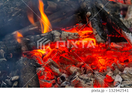 Glowing embers and flickering flames create a warm atmosphere in a campfire setting during a cool evening gathering Glowing embers and flickering flames create a warm atmosphere in a campfire setting during a cool evening gathering 132942541