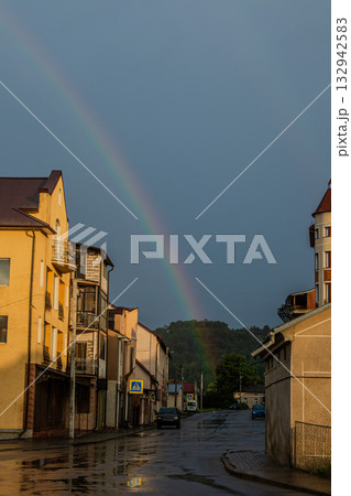 Rainfall gives way to a vibrant rainbow over a quiet street in a small town during evening light after a storm 132942583