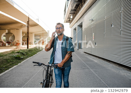 Male cyclist making phone call, standing by his bike. Male cyclist making phone call, standing by his bike. 132942979