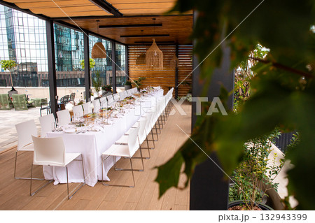 Long luxury banquet table set for event on modern rooftop terrace with greenery 132943399