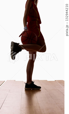 Female basketball player standing holding ball and stretching leg before game 132944210