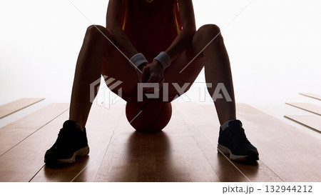 Female basketball player sitting with ball between knees in focus moment 132944212