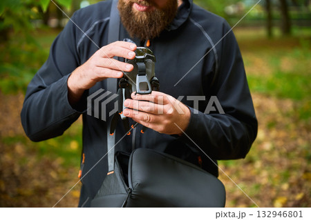 In a lush green park, a man adjusts his camera while standing among fallen leaves and vibrant trees. He focuses on capturing the beauty around him. In a lush green park, a man adjusts his camera while standing among fallen leaves and vibrant trees. He focuses on capturing the beauty around him. 132946801