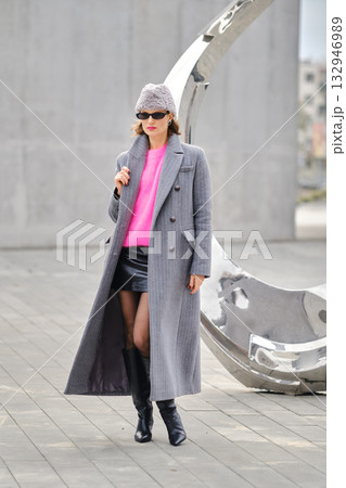 Urban street style features bold fashion with a long coat and bright top in a city setting Urban street style features bold fashion with a long coat and bright top in a city setting 132946989