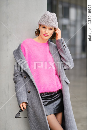 Urban street style highlights vibrant pink sweater and chic gray coat against modern backdrop Urban street style highlights vibrant pink sweater and chic gray coat against modern backdrop 132946995
